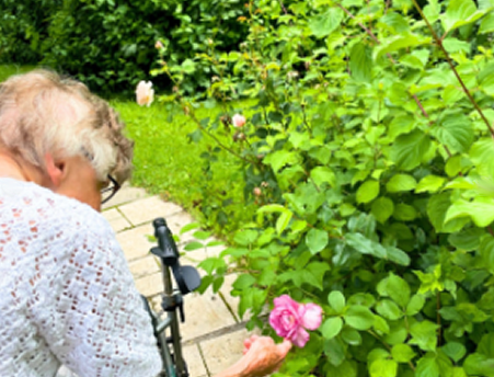 Eine Frau mit Rollator sieht sich eine Blume an.
