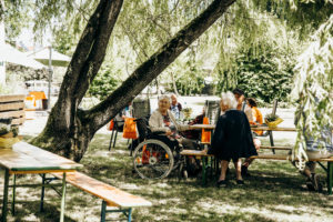 Ältere Menschen sitzen zusammen unter einem Baum im Garten