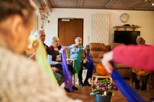 Menschen in einer Tagesbetreuung sitzen in einem Kreis und machen motorische Übungen