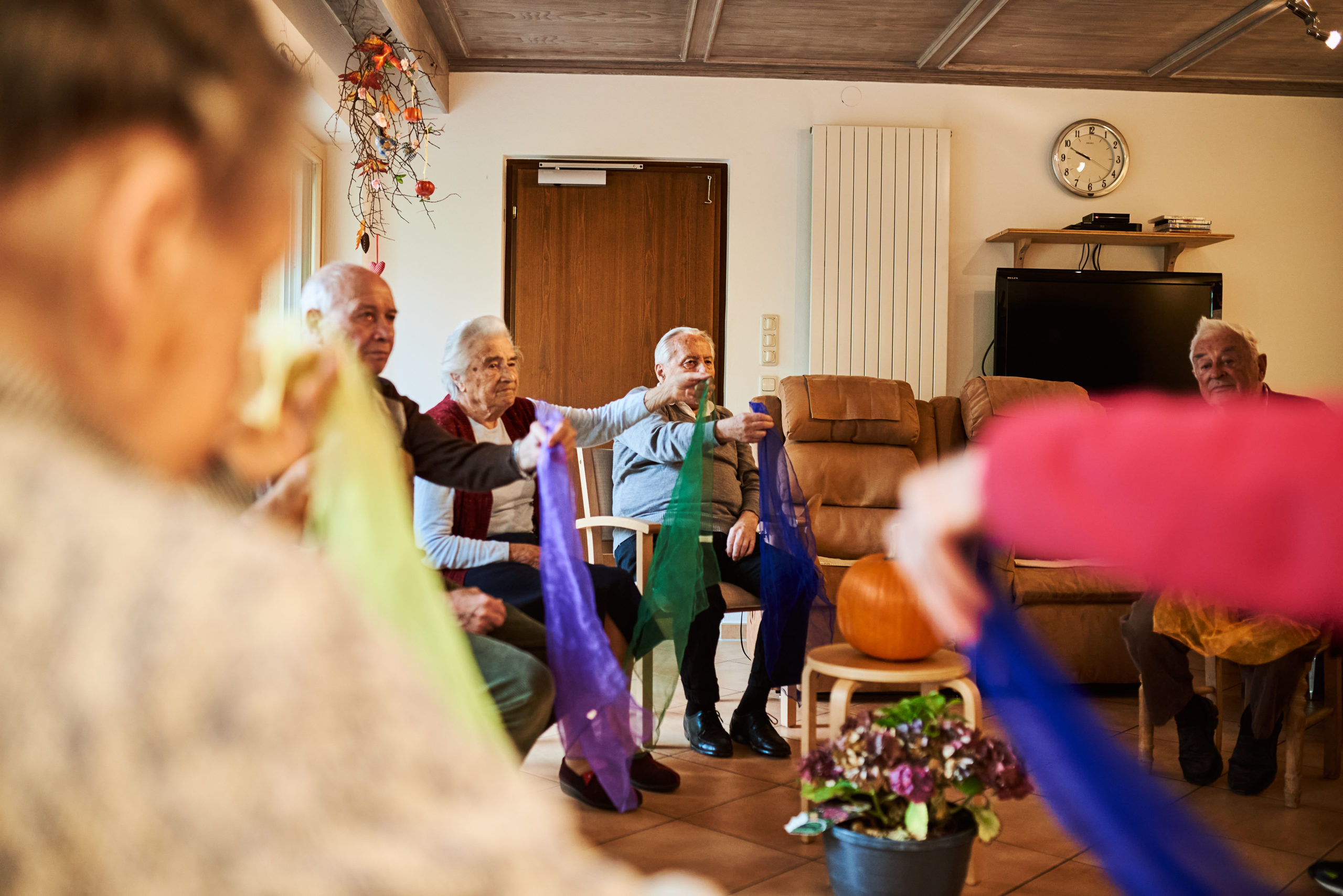 Menschen in einer Tagesbetreuung sitzen in einem Kreis und machen motorische Übungen