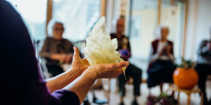 Die Besucher der Sophia-Tagesbetreuung sitzen in einem Kreis und halten der Reihe nach ein leichtes Tuch, das zu einer Art Ball geformt ist.